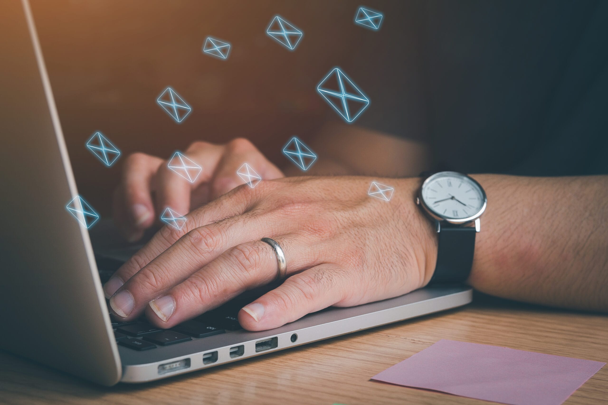 Човек пише на лаптоп, от който излизат много икони на имейли.